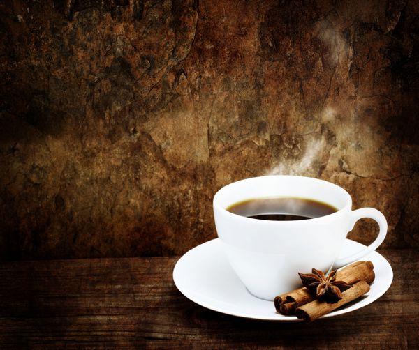 فنجان قهوه داغ در لیوان سفید با دارچین و بادیان ستاره ای در گرانج - سبک قدیمی