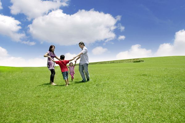 خانواده آسیایی خوشحال در حال بازی در زمین آنها به صورت دایره ای می دوند که بر فراز آسمان آبی عکس گرفته شده است