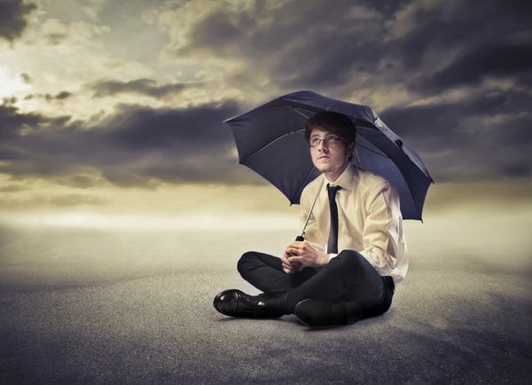 تاجر جوان زیر یک چتر با آسمان طوفانی در پس زمینه
