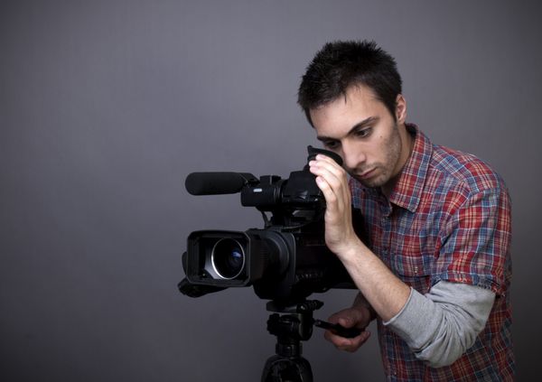 عکس استودیویی از مرد جوان با دوربین فیلمبرداری در پس زمینه خاکستری با فضای کپی
