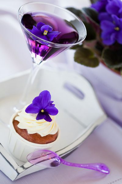 کیک کوچک تزئین شده با خامه فرم گرفته و گل بنفشه و کوکتل فوکوس انتخابی