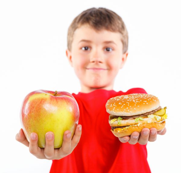 پسر ناز در حال خوردن یک سیب یا همبرگر روی سیب و همبرگر تمرکز کنید جدا شده بر روی پس زمینه سفید