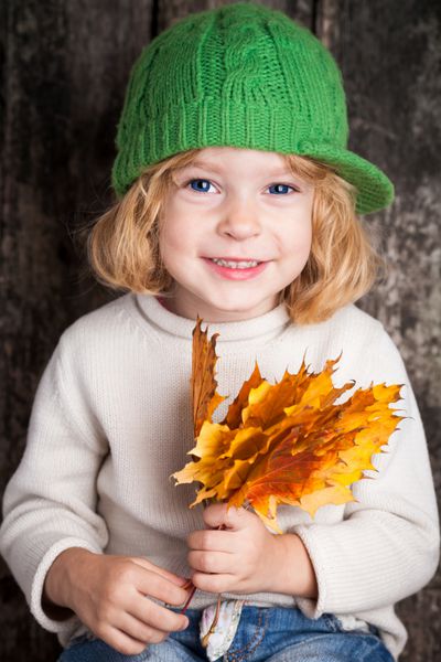بچه خندان بامزه که برگ های افرا زرد را در دست دارد مفهوم پاییز