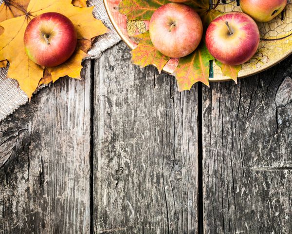 حاشیه پاییزی از سیب و برگ های افتاده روی میز چوبی قدیمی مفهوم روز شکرگزاری