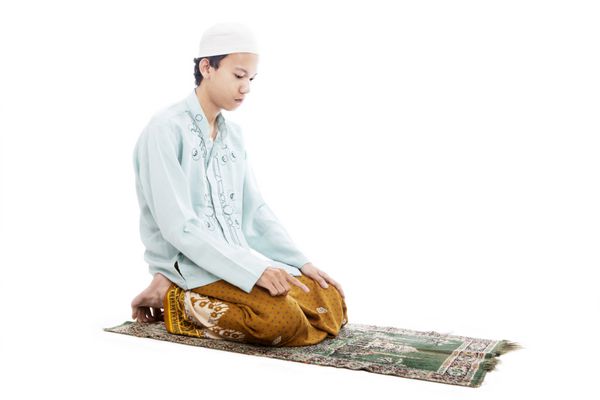 پرتره مرد مسلمان آسیایی که روی حصیر نماز می خواند در استودیو جدا شده روی سفید عکس گرفته شده است