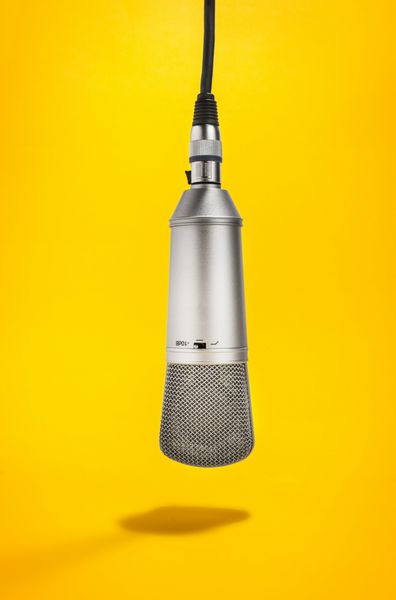 یک میکروفون استودیویی ایزوله که از بالا با سیم آن رو به پایین روی پس‌زمینه زرد آویزان است