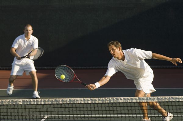 بازیکن دونفره مختلط در حال ضربه زدن به توپ تنیس با شریک در پس زمینه