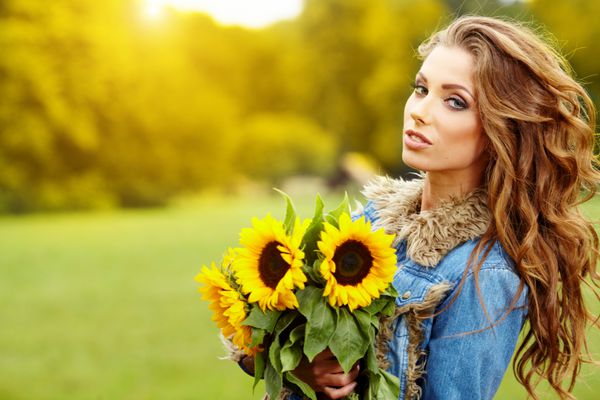 زن جوان مد با یک دسته گل آفتابگردان در مزرعه