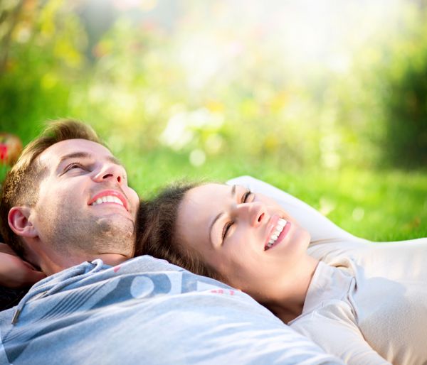 زوج خندان خوشحال در حال استراحت روی چمن سبز پارک زوج جوان دراز کشیده روی چمن در فضای باز