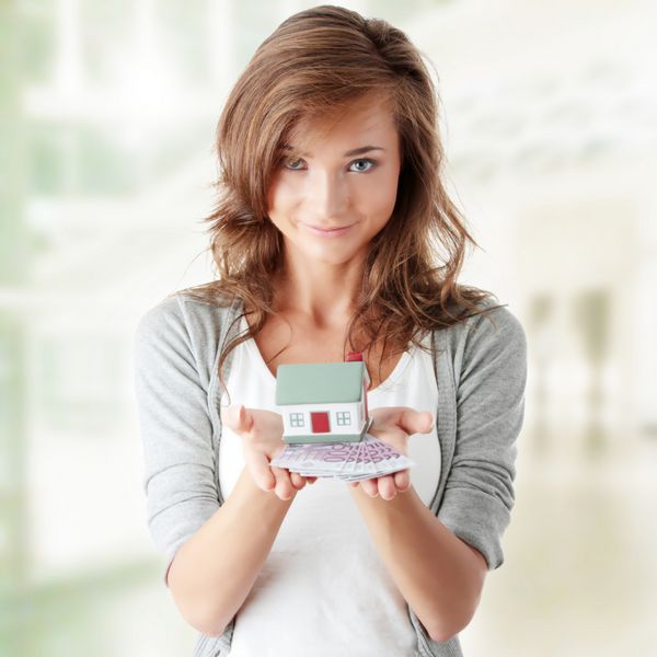 زن جوان زیبا که اسکناس های یورو و مدل خانه را روی سفید نگه می دارد - مفهوم وام املاک و مستغلات