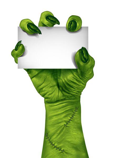دست زامبی که یک کارت علامت خالی را به‌عنوان نماد ترسناک یا ترسناک هالووین با پوست سبز بافت انگشتان هیولایی چروکیده و بخیه‌های جدا شده روی پس‌زمینه سفید در دست دارد