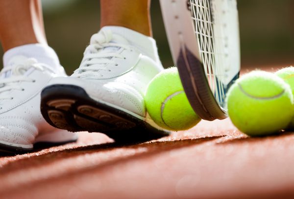 پاهای دختر ورزشکار در نزدیکی راکت تنیس و توپ