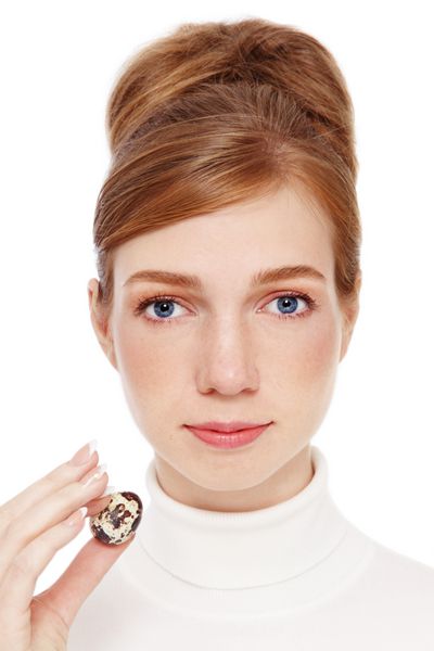 دختر جوان مو قرمز با کک و مک که تخم بلدرچین را در دست دارد در پس زمینه سفید