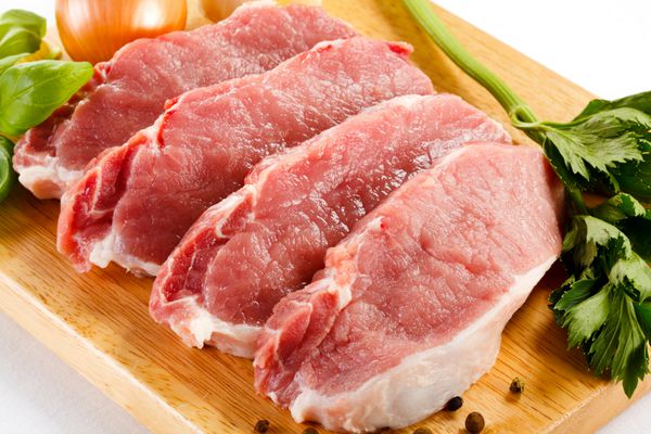 گوشت خوک خام روی تخته برش و سبزیجات