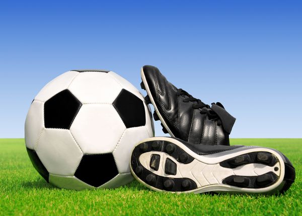 توپ فوتبال و کفش در چمن