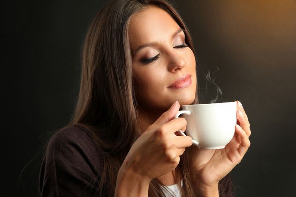 زن جوان زیبا با فنجان قهوه در پس زمینه قهوه ای