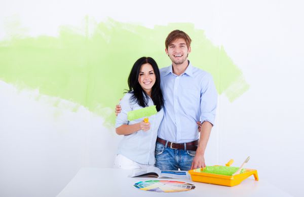 زوج جوان شاد دیوار خانه آپارتمان جدید خود را به رنگ سبز رنگ سفید می کنند