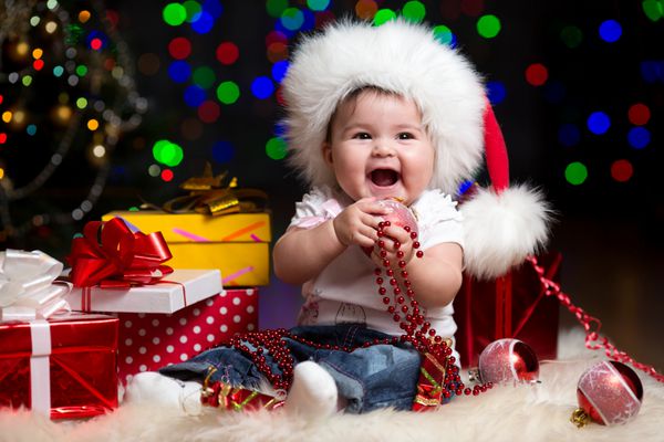 کودک خنده دار با کلاه بابا نوئل در پس زمینه جشن روشن