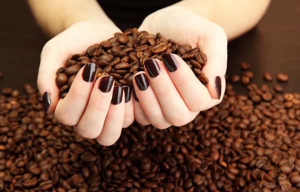 دست های زن با دانه های قهوه از نزدیک