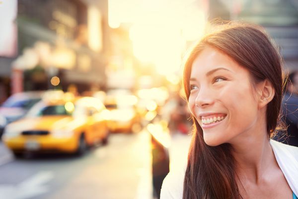 زن آسیایی سرزنده در شهر نیویورک با یک لبخند درخشان زیبا با نور پس‌زمینه درخشش گرم خورشید که در خیابانی شلوغ با تاکسی‌ها در مرکز شهر منهتن شهر نیویورک می‌تابد