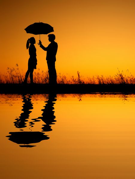 انعکاس زن و مردی که چتر در دست دارند در شبح غروب عصر