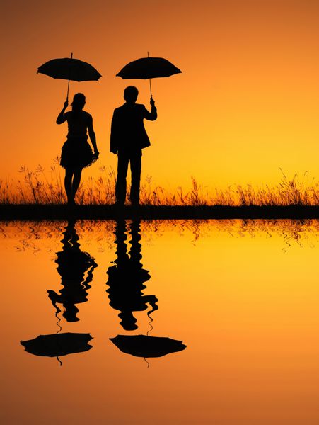 انعکاس زن و مردی که چتر در دست دارند در شبح غروب عصر