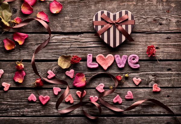 جعبه هدیه روز ولنتاین به شکل قلب در بشقاب های چوبی قدیمی پس زمینه شیرین تعطیلات با گلبرگ های رز قلب های کوچک روبان منحنی