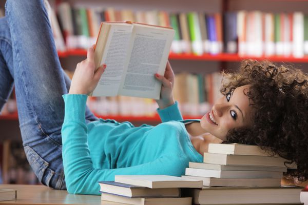 پرتره دختر دانشجوی زیبا در کتابخانه در حال خواندن کتاب