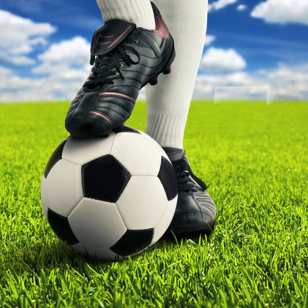 پاهای بازیکن فوتبال در حالت گاه به گاه در زمین بازی باز با آسمان در پس زمینه