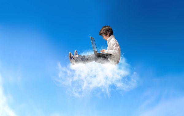 پسر جوان با لپ تاپ که روی ابری در آسمان نشسته است