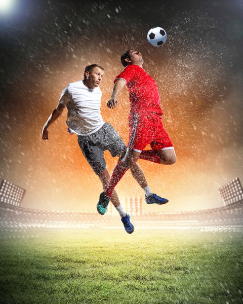 دو بازیکن فوتبال برای ضربه زدن به توپ در ورزشگاه می پرند