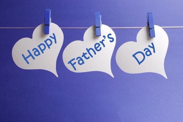 پیام تبریک روز پدر که روی برچسب‌های قلبی سفید نوشته شده است که از گیره‌های آبی روی خطی در مقابل پس‌زمینه آبی آویزان شده‌اند