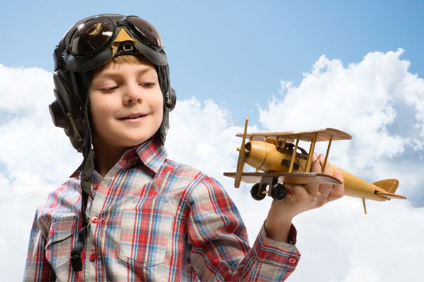 پسر خلبان کلاه ایمنی در حال بازی با یک هواپیمای چوبی اسباب بازی در ابرها در آرزوی خلبان شدن