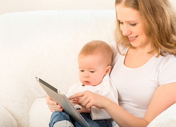 مادر و نوزاد به دنبال بازی و خواندن رایانه لوحی روی مبل در خانه هستند