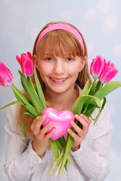 پرتره خنده دار دختر جوان زیبا که دسته گل لاله صورتی و قلب در دست دارد