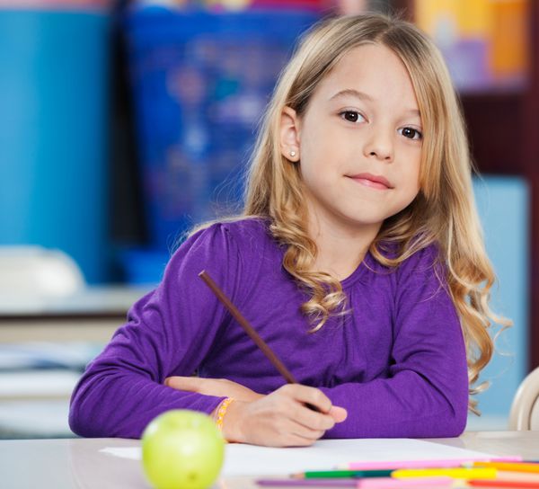 پرتره دختر کوچولوی ناز با قلم و کاغذ طرح روی میز کلاس