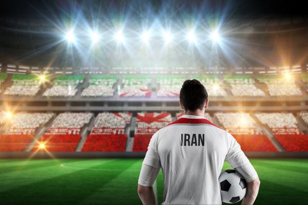 بازیکن فوتبال ایران در حال نگه داشتن توپ در مقابل ورزشگاه پر از هواداران فوتبال ایران