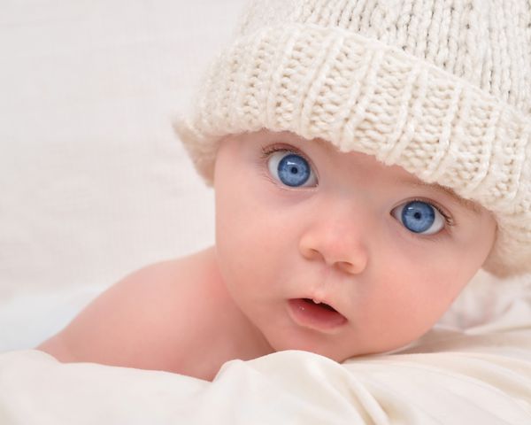 یک بچه کوچولوی ناز به دوربین نگاه می کند و کلاه سفیدی بر سر دارد نوزاد می تواند پسر یا دختر باشد و چشمان آبی داشته باشد از آن برای مفهوم فرزندپروری یا عشق استفاده کنید