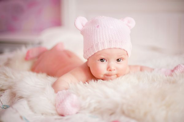 دختر بچه تازه متولد شده با کلاه خرس بافتنی صورتی روی خز خوابیده است