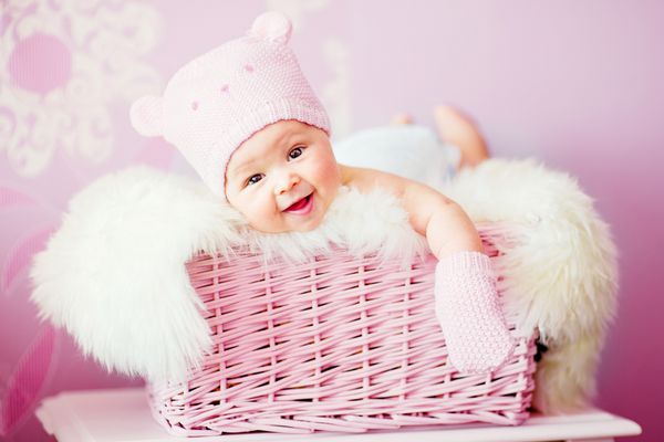 دختر نوزاد تازه متولد شده با کلاه خرس بافتنی صورتی در سبد خوابیده است