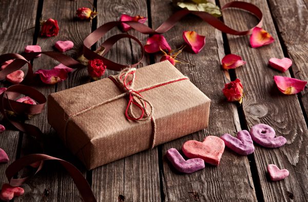 Word Love با جعبه هدیه روی بشقاب های چوبی قدیمی پس زمینه شیرین تعطیلات - گلبرگ های رز قلب های کوچک روبان منحنی و غیره