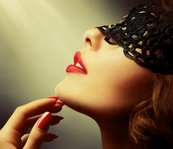 زن زیبا با ماسک توری سیاه روی چشم هایش نمای قرمز لب ها و ناخن ها
