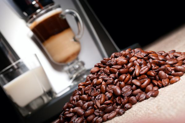 کپه دانه های قهوه و دستگاه قهوه با شیر و لیوان لاته