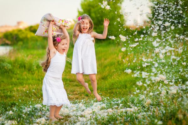 کودکی شاد دختران کوچک که با بالش و پر سرگرم می شوند