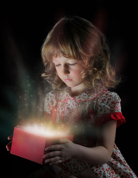 دختر لبخند می زند و هدیه ای در بسته بندی جادویی در پس زمینه مشکی در دست دارد