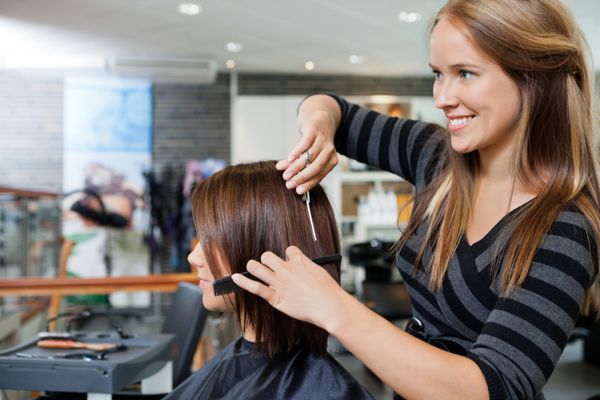 آرایشگر جوان زیبا که یک مدل موی جدید به مشتری زن در سالن آرایش می دهد
