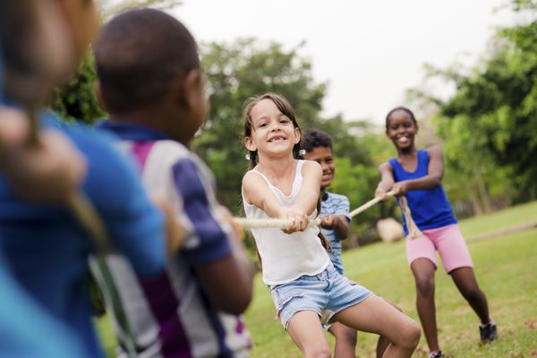 کودکان و تفریحات گروهی از بچه های مدرسه چند قومیتی شاد که در پارک شهر طناب کشی می کنند سرگرمی کمپ تابستانی