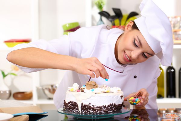 زن جوان سرآشپز در حال پختن کیک در آشپزخانه