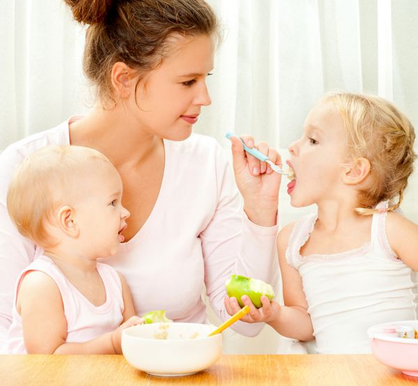 مادر جوانی که با قاشق به دو دخترش غذا می دهد