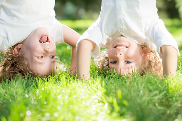 کودکان شادی که وارونه روی چمن سبز در پارک بهار ایستاده اند مفهوم سبک زندگی سالم